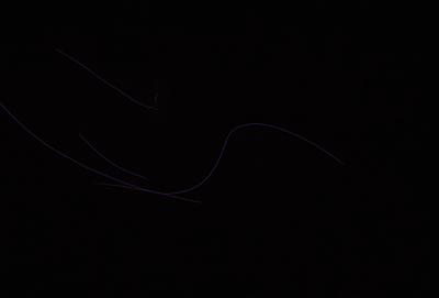 The primary subject of the image is a purple line or curve, which appears to be a part of a larger pattern or design. The setting is a dark background, which contrasts with the purple line. The visual style of the image is a combination of a photo and a digital art or illustration, as the purple line is both distinct and integrated into the overall composition. The colors and mood of the image are predominantly dark and moody, with the purple line serving as a focal point amidst the darkness
