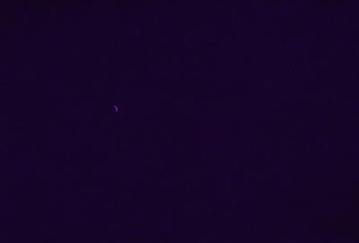 The image is a black and white photo of a night sky. The primary subject is a crescent moon, which is visible in the upper left corner of the image. The setting is a dark, star-filled sky, with no other objects or landmarks visible. The visual style is a traditional, artistic representation of the night sky. The colors and mood of the image are predominantly dark and moody, with the moon being the only bright spot in the sky.