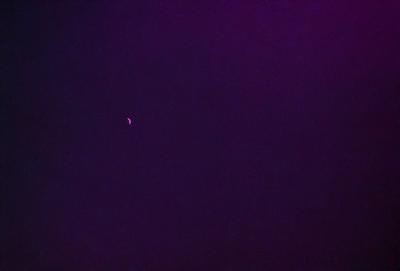 The primary subject of the image is a small, bright moon in the dark sky. The setting is a vast, starry night with a purple hue. The visual style is a realistic representation of the moon and the night sky. The colors and mood convey a sense of tranquility and wonder as the moon shines brightly against the dark backdrop.