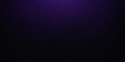 The image is a black and white photo of a dark, purple sky. The sky is filled with stars, creating a sense of depth and a serene atmosphere. The primary subject is the sky, which serves as the backdrop for the stars. The visual style is a photo, and the colors and mood are predominantly dark and moody, with the purple hue adding a touch of mystery to the scene.