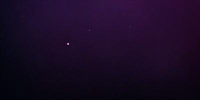 The image features a dark, purple sky with a few stars visible. The primary subject is the night sky, which is the setting and background of the image. The visual style is a photo, capturing the beauty of the night sky. The colors and mood of the image are predominantly dark and moody, with the purple hue adding a sense of mystery to the scene.