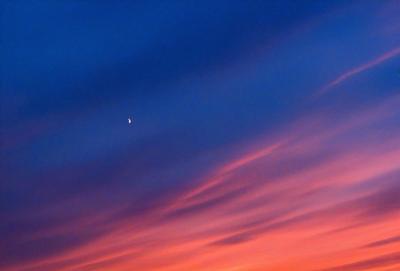 The primary subject of the image is a moon, which is visible in the sky. The setting is a beautiful sunset, with the sky filled with vibrant colors. The visual style of the image is a photo, capturing the stunning view of the moon and the sunset. The dominant colors in the image are orange, pink, and blue, creating a warm and serene atmosphere.