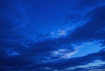 The primary subject of the image is a cloudy blue sky. The setting is a nighttime scene with a dark blue sky, and the visual style is a photo. The colors and mood of the image are predominantly dark and moody, with the blue hues of the sky creating a sense of calmness.