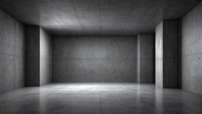 The primary subject of the image is a large, empty room with a concrete wall. The setting is a dark, empty space, and the visual style is a black and white photo. The room appears to be a large, open area with no furniture or decorations, giving it a stark and minimalist appearance. The dominant colors are black and white, creating a moody and dramatic atmosphere.