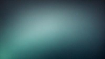 The image features a large, dark blue wall with a green tint. The primary subject is a single, small dot located in the upper right corner of the wall. The visual style appears to be a photo, and the colors and mood convey a sense of depth and mystery.