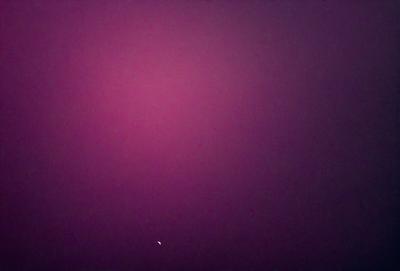 The primary subject of the image is a pink background, which appears to be a purple sky. The setting is a dark, cloudy sky, creating a moody atmosphere. The visual style is a photo, capturing the unique color and texture of the sky. The colors and mood of the image are predominantly dark and dramatic, with the pink or purple hue adding a touch of warmth to the scene.
