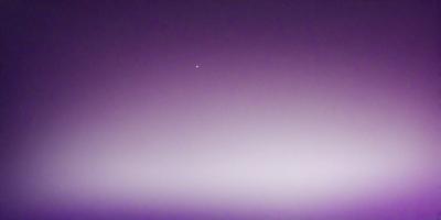 The primary subject of the image is a single star in the night sky. The setting is a dark, purple-colored sky, which creates a dramatic and moody atmosphere. The visual style of the image is a photo, capturing the star and its surroundings. The colors and mood of the image are predominantly purple, with the star being the main focal point against the dark, starry sky.