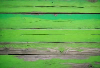 The primary subject of the image is a green wooden surface, possibly a fence or a wall. The setting is outdoors, with a natural environment visible in the background. The visual style is a close-up of the wooden surface, showcasing its texture and color. The dominant colors are green, which creates a calm and serene atmosphere.