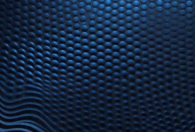 The primary subject of the image is a blue surface with a pattern of small circles. The setting is a dark room, and the visual style appears to be a close-up of the blue surface. The dominant colors are blue and black, creating a calm and soothing atmosphere.