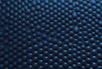 The primary subject of the image is a blue surface with a pattern of black circles. The setting appears to be a dark room, and the visual style is a close-up of the blue surface. The dominant colors are blue and black, creating a moody atmosphere.