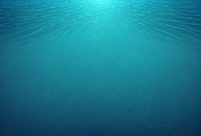 The primary subject of the image is a large body of water, which appears to be a deep blue ocean. The setting is underwater, with the water surface visible. The visual style is a photo, capturing the beauty of the ocean. The colors and mood are predominantly blue, creating a serene and tranquil atmosphere.