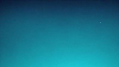 The primary subject of the image is the night sky, which is filled with stars. The setting is a dark, star-filled sky, and the visual style is a photo. The colors and mood of the image are predominantly dark and serene, with the stars providing a sense of depth and beauty.