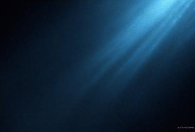 The primary subject of the image is a blue background with a light source, possibly a sun or a light bulb, shining through it. The light source creates a bright and shiny effect on the blue background. The setting appears to be a dark room, as the light source is the only visible element in the image. The visual style of the image is a combination of a photo and a digital art, as it captures the light source's reflection on the blue background. The colors and mood of the image are predominantly