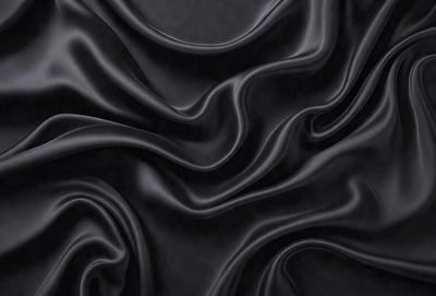 The primary subject of the image is a close-up of a black fabric, possibly a piece of clothing or a curtain. The setting is a dark background, which emphasizes the fabric's texture and pattern. The visual style appears to be a photo, as it captures the details of the fabric. The colors and mood of the image are predominantly dark, with the black fabric being the main focus.