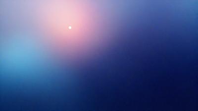 The primary subject of the image is a sunset, with the sun visible in the sky. The setting is a dark blue sky, which contrasts with the warm hues of the sunset. The visual style is a photo, capturing the beauty of the sunset. The colors and mood of the image are serene and calming, as the sun sets and the sky transitions from day to night.