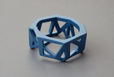 The primary subject of the image is a blue geometric bracelet. The setting is a white background, which provides a clean and minimalist appearance. The visual style is a digital art, as the bracelet is depicted in a 3D model. The colors and mood of the image are predominantly blue, giving it a modern and stylish look.