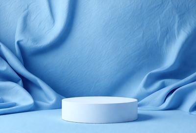 The primary subject of the image is a white, round, flat object, possibly a plate or a bowl, placed on a blue surface. The setting appears to be a studio or a similar indoor environment. The visual style of the image is a photo, capturing the details of the white object on the blue background. The colors and mood of the image are predominantly blue, creating a calm and serene atmosphere.