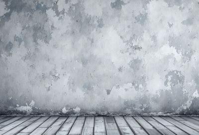 The primary subject of the image is a large, dirty, and weathered concrete wall. The setting is a room with a wooden floor, and the visual style is a black and white photo. The colors and mood of the image are dark and moody, with the concrete wall and wooden floor creating a sense of age and wear.