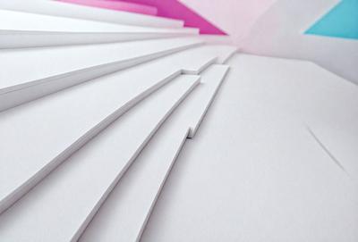 The primary subject of the image is a stack of white paper. The setting is a pink background, which adds a contrasting color to the scene. The visual style is a close-up of the paper, showcasing its texture and details. The colors and mood of the image are predominantly white, giving it a clean and minimalist appearance.
