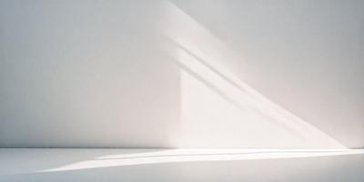 The primary subject of the image is a white wall with a shadow cast on it. The setting is a room with a window, and the visual style appears to be a photo. The colors in the image are predominantly white, giving it a clean and minimalist appearance. The mood of the image is calm and serene, as the light from the window creates a peaceful atmosphere.