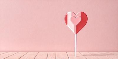 The primary subject of the image is a heart-shaped candy on a pink background. The heart is red and white, and it is placed on a pink surface. The setting appears to be a pink wall, and the visual style is a close-up of the heart-shaped candy. The colors and mood of the image are predominantly pink, creating a warm and inviting atmosphere.