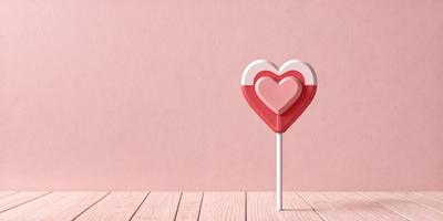 The primary subject of the image is a heart-shaped candy on a pink background. The heart is red and white, and it is placed on a white stick. The setting is a pink wall, which provides a contrasting background for the heart-shaped candy. The visual style of the image is a close-up of the heart-shaped candy, emphasizing its shape and color. The colors and mood of the image are predominantly pink and warm, creating a sense of love and affection