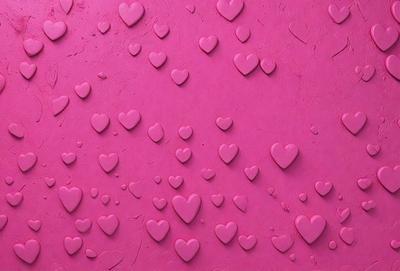 The primary subject of the image is a pink surface with numerous hearts scattered across it. The hearts are of various sizes and are placed in different positions on the pink surface. The setting appears to be a pink background, and the visual style is a close-up of the hearts on the pink surface. The colors and mood of the image are predominantly pink, creating a warm and inviting atmosphere.