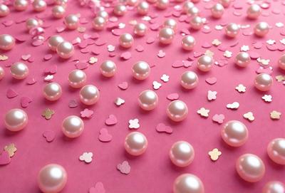 The primary subject of the image is a pink background with a scattering of pink and white pearls. The setting appears to be a pink table or surface, and the visual style is a close-up of the pearls on the pink background. The colors and mood of the image are predominantly pink and white, creating a warm and inviting atmosphere.