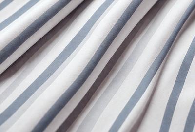 The primary subject of the image is a striped fabric, which is the main object, scene, or focus of the image. The setting or background consists of a white surface, possibly a wall or a table. The visual style of the image is a close-up of the striped fabric, showcasing its texture and pattern. The colors and mood of the image are predominantly white and gray, giving it a clean and minimalist appearance.