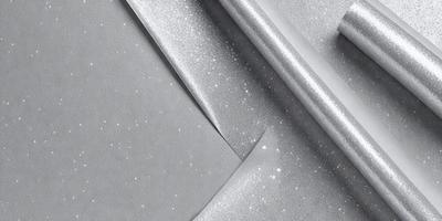 The primary subject of the image is a piece of silver fabric. The setting is a room with a table, and the visual style is a close-up of the fabric. The colors and mood of the image are predominantly silver and metallic, giving it a shiny and reflective appearance.