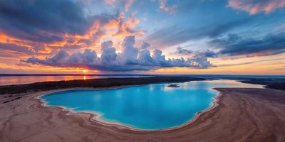 The primary subject of the image is a large body of water, which appears to be a lagoon or a lake. The water is a deep blue color, and it is surrounded by a beautiful landscape. The setting includes a beach, a mountain, and a cloudy sky. The visual style of the image is a photo, capturing the natural beauty of the scene. The colors and mood of the image are serene and peaceful, with the deep blue water and the surrounding landscape creating a calming atmosphere.