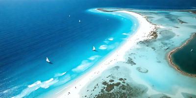 The primary subject of the image is a beach scene with a large body of water and a sandy shore. The setting includes a clear blue ocean and a sandy beach. The visual style of the image is a photo, capturing the natural beauty of the beach and the ocean. The colors and mood of the image are predominantly blue and serene, creating a peaceful and relaxing atmosphere.