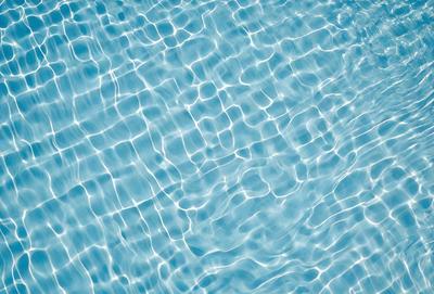 The primary subject of the image is a large body of water, possibly a swimming pool, with a blue color. The water appears to be rippling and has a clear, blue appearance. The setting is a swimming pool, and the visual style is a photo. The colors and mood of the image are predominantly blue, creating a calm and serene atmosphere.