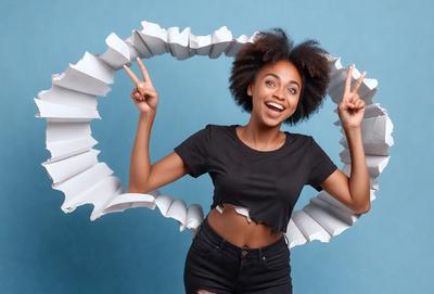 The primary subject of the image is a woman with a smile on her face, posing for a picture. She is wearing a black shirt and black pants. The setting is a blue background, and the visual style appears to be a photo. The woman is the main focus of the image, and her smile and pose create a positive and cheerful atmosphere.