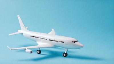 The primary subject of the image is a white model airplane. The airplane is placed on a blue surface, which serves as the background. The visual style of the image is a photo, capturing the details of the model airplane. The colors and mood of the image are predominantly white and blue, creating a clean and calm atmosphere.