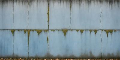 The primary subject of the image is a blue wall with a cracked and peeling surface. The setting is an outdoor environment, with the wall being the main object of focus. The visual style is a photo, capturing the cracked and peeling wall in detail. The colors and mood of the image are predominantly blue, with a slightly dull and aged appearance due to the cracked and peeling surface.