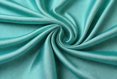 The primary subject of the image is a close-up of a blue fabric, possibly a piece of silk or a similar material. The setting is a room with a blue background, which complements the blue fabric. The visual style is a close-up, focusing on the details of the fabric. The colors and mood of the image are predominantly blue, creating a calm and serene atmosphere.
