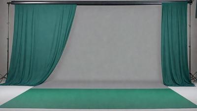 The primary subject of the image is a green curtain hanging on a wall. The setting is a plain white wall, which serves as the background. The visual style of the image is a photo, capturing the curtain in its natural environment. The colors and mood of the image are predominantly green, creating a calm and serene atmosphere.