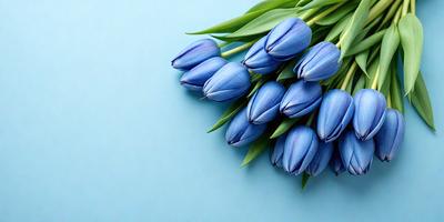 The primary subject of the image is a bouquet of blue flowers, which are the main focus of the scene. The flowers are arranged in a vase and are placed on a blue surface, which adds a contrasting and visually appealing backdrop to the scene. The visual style of the image is a photo, capturing the beauty and details of the flowers. The dominant colors in the image are blue and green, creating a serene and calming atmosphere.