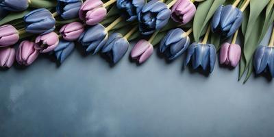 The primary subject of the image is a bouquet of purple and blue tulips. The setting is a blue background, which creates a visually appealing contrast with the vibrant colors of the flowers. The visual style is a close-up of the flowers, showcasing their details and beauty. The colors and mood of the image are predominantly purple and blue, giving it a calm and serene atmosphere.