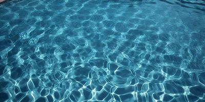 The primary subject of the image is a swimming pool filled with blue water. The setting is an outdoor environment, with the pool being the main object of focus. The visual style is a photo, capturing the reflections and ripples of the water. The colors and mood of the image are predominantly blue, creating a calm and serene atmosphere.