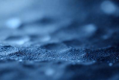 The primary subject of the image is a blue surface with a pattern of bubbles or droplets. The setting appears to be a dark, possibly underwater environment. The visual style of the image is a close-up of the blue surface, which gives a sense of depth and texture. The colors and mood of the image are predominantly blue, creating a calm and serene atmosphere.