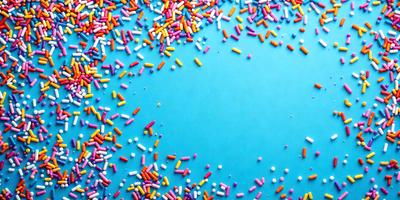 The primary subject of the image is a close-up of a blue surface with a pattern of colorful sprinkles. The setting is a table with a blue background. The visual style is a photo, and the colors and mood are vibrant and cheerful.