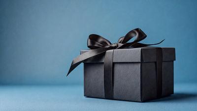 The primary subject of the image is a black box with a black bow on top. The setting is a blue background, which creates a contrasting and visually appealing scene. The visual style is a close-up of the box, showcasing the details of the bow and the box itself. The colors and mood of the image are predominantly dark, with the black box and bow creating a sense of elegance and sophistication.