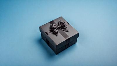 The primary subject of the image is a black box with a bow on top. The box is placed on a blue surface, which serves as the setting or background. The visual style of the image is a photo, capturing the details of the box and the bow. The colors in the image are predominantly black and blue, creating a sense of elegance and sophistication.