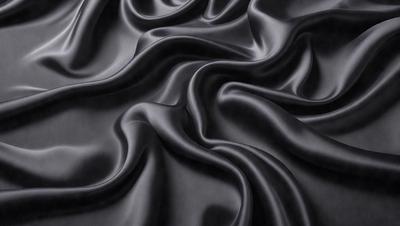The primary subject of the image is a close-up of a black fabric, possibly a piece of clothing or a curtain. The setting is a dark background, which emphasizes the fabric's texture and pattern. The visual style appears to be a photo, as it captures the details of the fabric. The colors and mood of the image are predominantly dark, with the black fabric being the main focus.