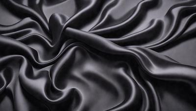The primary subject of the image is a black fabric, which appears to be a piece of clothing or a curtain. The setting is a dark room, and the visual style is a close-up of the fabric. The colors and mood of the image are predominantly dark and moody, with the black fabric being the main focus.