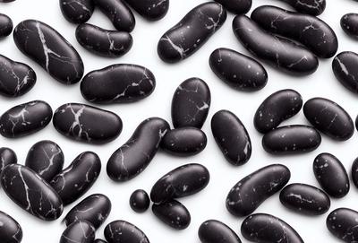 The primary subject of the image is a collection of black beans. They are arranged in a pattern on a white surface, creating a visually appealing display. The beans are the main focus of the image, and their contrast with the white background adds a striking visual effect. The overall atmosphere of the image is clean, simple, and elegant.