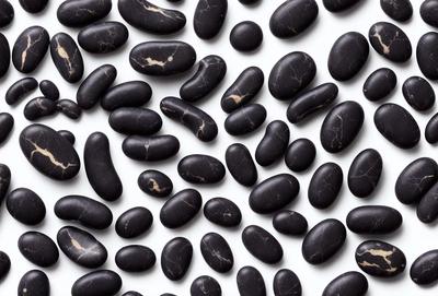 The primary subject of the image is a large collection of black beans. The beans are arranged in a pattern, covering the entire image. The setting is a white background, which provides a clean and uncluttered look to the scene. The visual style is a close-up of the beans, showcasing their details and texture. The colors and mood of the image are predominantly black, giving it a bold and striking appearance.