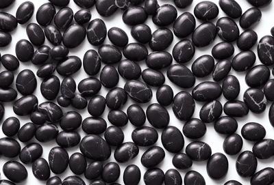 The primary subject of the image is a large collection of black beads, which are arranged in a visually appealing manner. The setting is a white background, which provides a clean and uncluttered environment for the beads. The visual style of the image is a close-up of the beads, showcasing their intricate details. The colors and mood of the image are predominantly black, giving it a sleek and modern appearance.